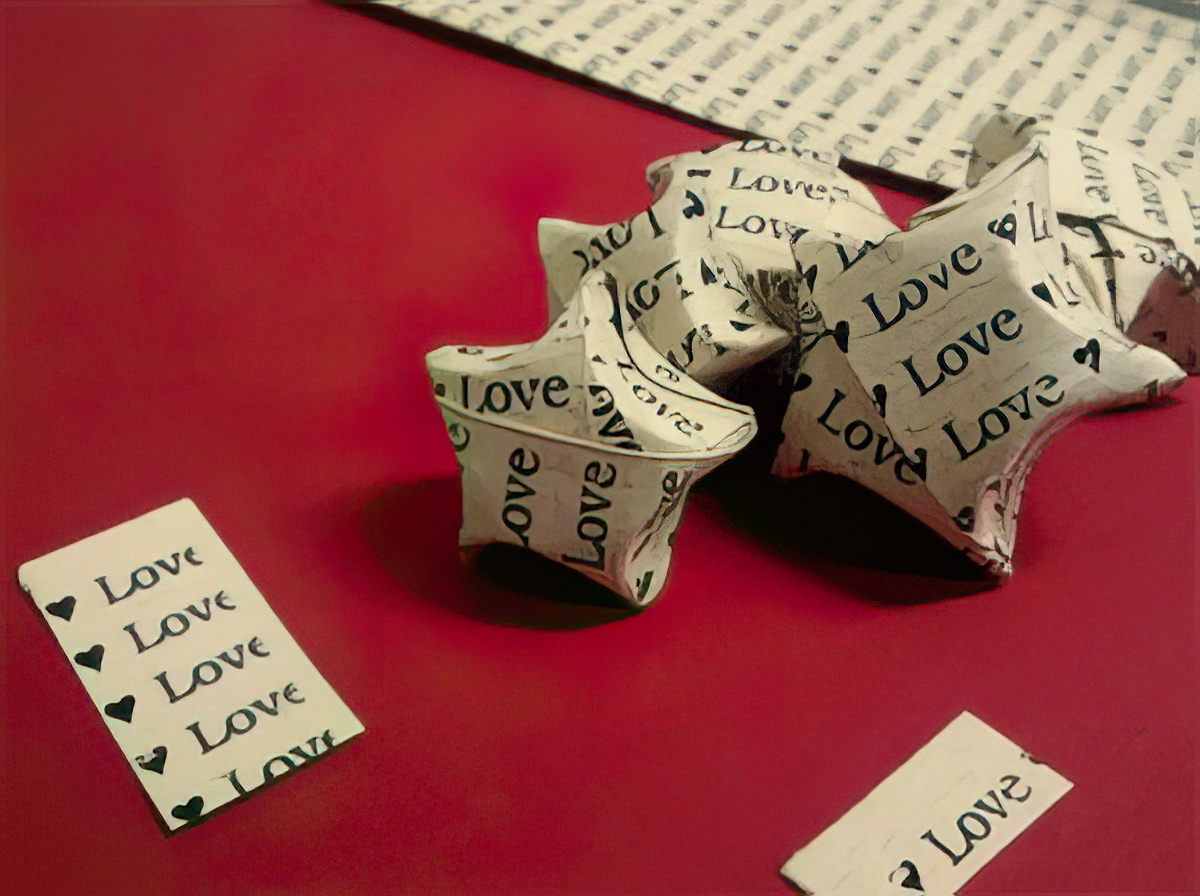 Love” printed repeatedly in different orientations against a red background. Small rectangular paper snippets also display the same “Love” print, scattered around the stars. The pattern of “Love” print and the origami stars suggest a theme of affection and handmade art.